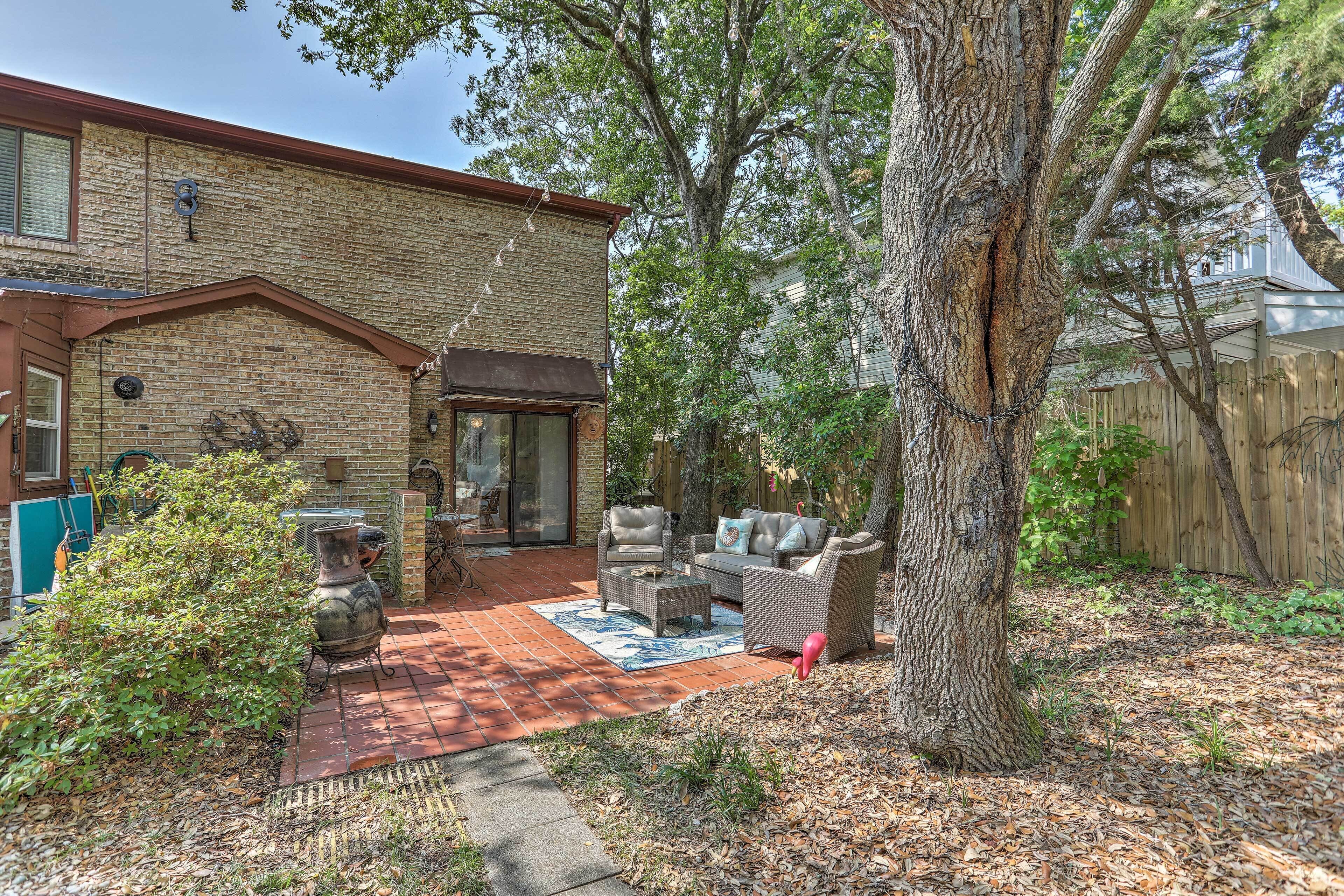 A brick house with a patio, outdoor furniture, and a large tree.