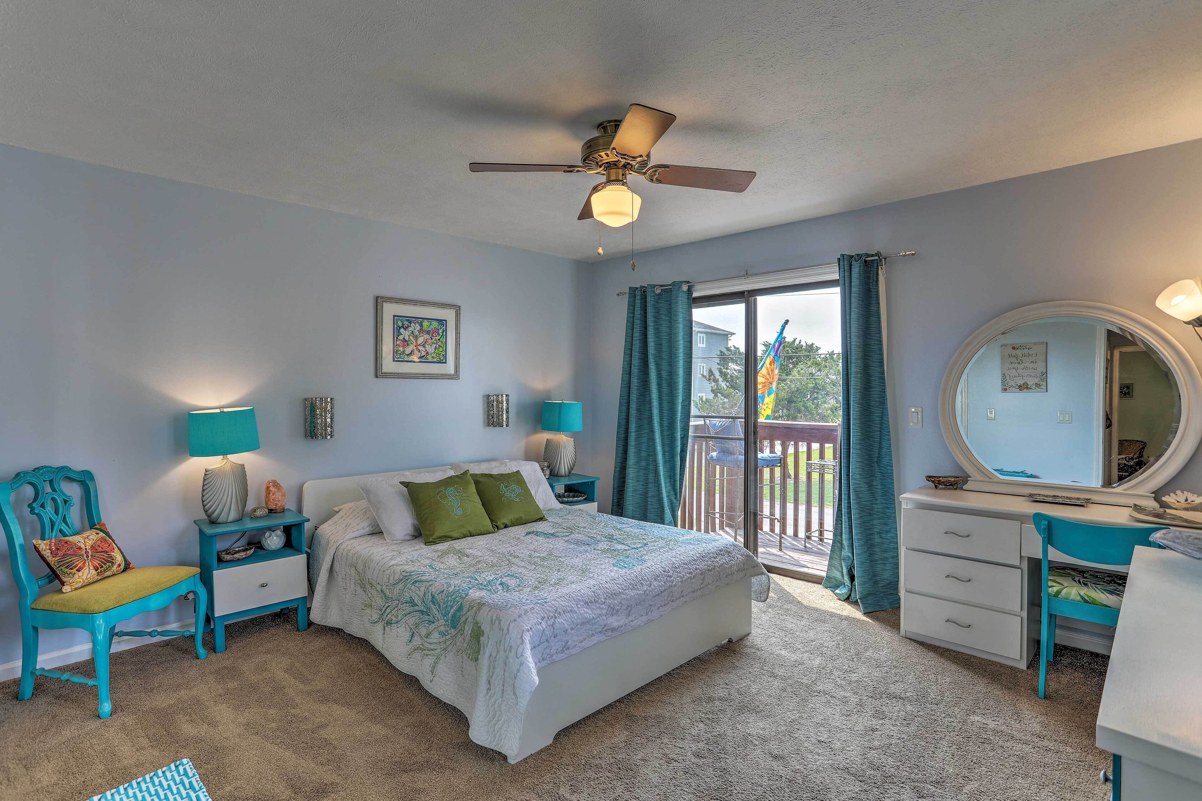 A bedroom with a bed, a desk, a chair, a dresser, a ceiling fan, and a window with curtains.