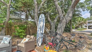 Ein Garten mit einem Korbstuhl, einem Surfbrett, einem Fahrrad und einem bunten Tiki-Sonnenschirm.