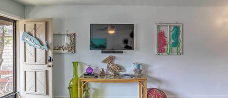 A room with a wooden door, a glass-top table with decorative items, a television, and wall art.