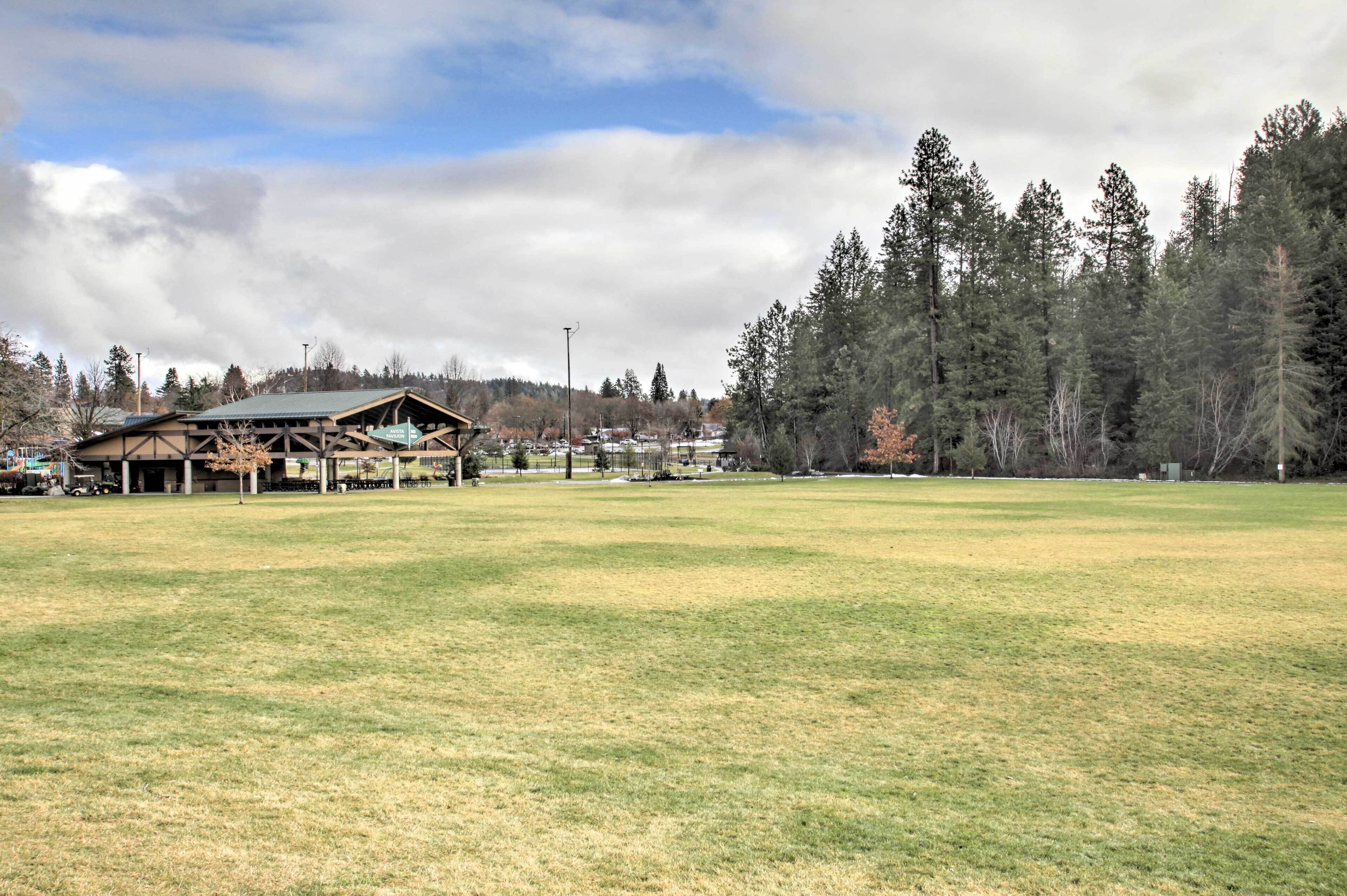 A large open grassy field with a wooden structure and a forest in the background.