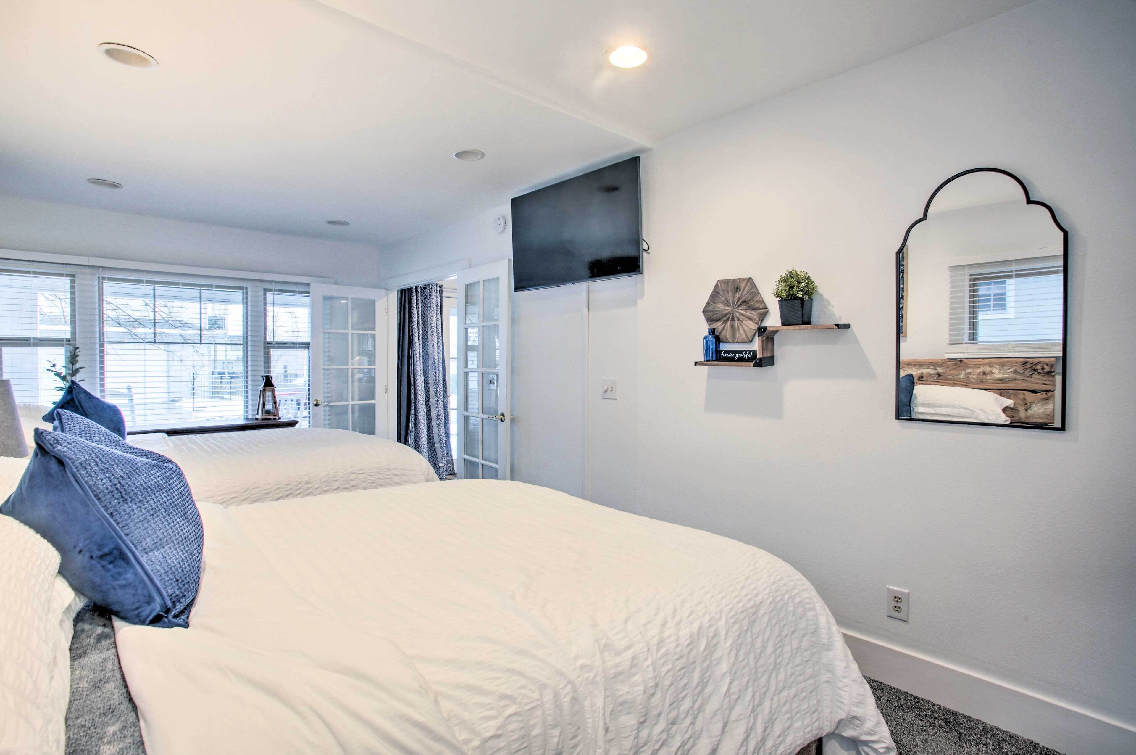 A bedroom with two beds, a TV, a mirror, and a window with blinds.