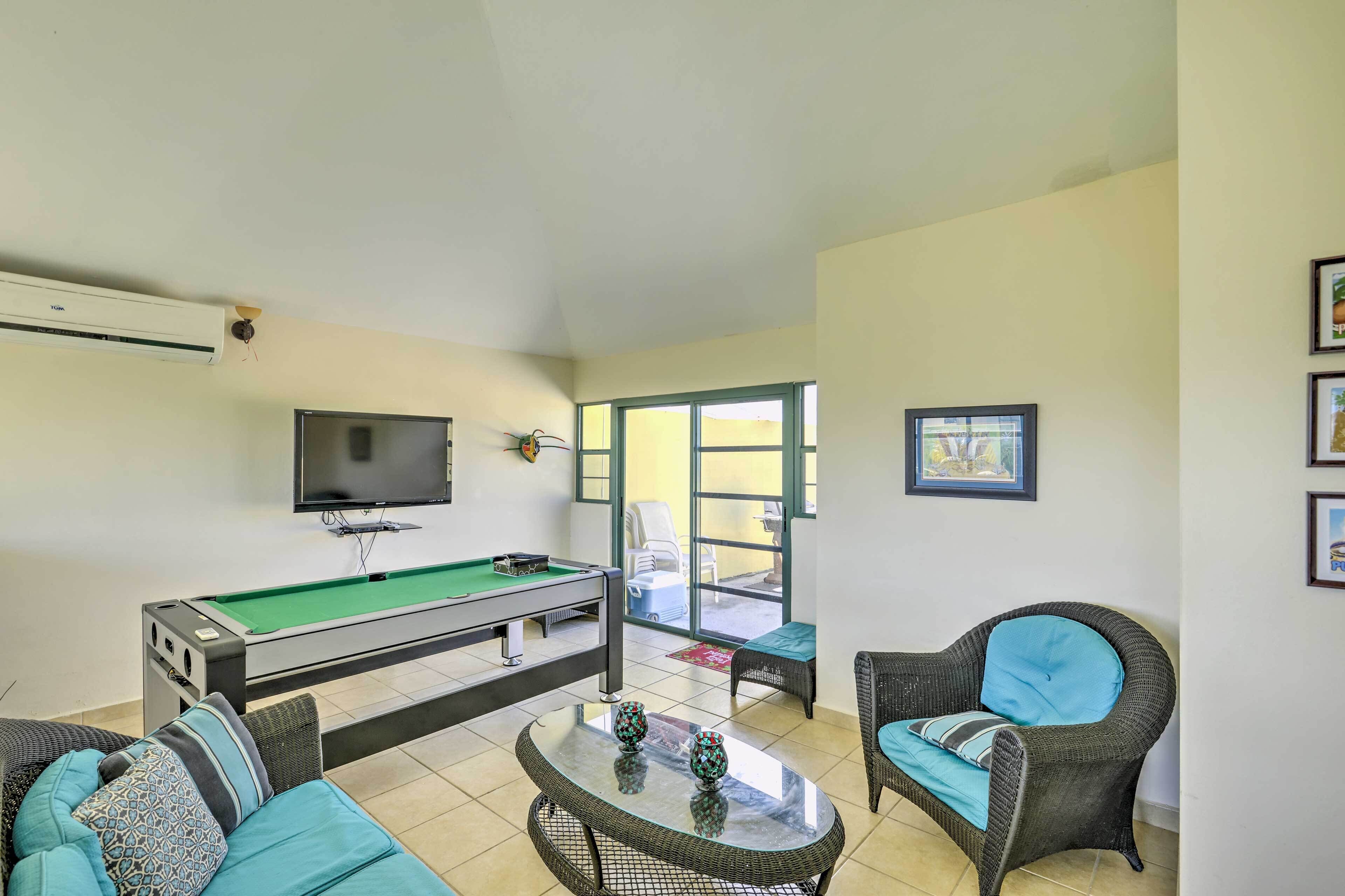 Une pièce équipée d’une table de billard, d’un téléviseur, de meubles en osier et d’une porte donnant sur un espace extérieur.