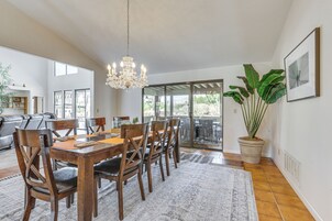 A dining area with a wooden table and chairs, a chandelier, a large potted plant, and a sliding glass door leading to an outdoor patio.