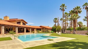 Una casa con piscina, patio y jardín con palmeras.