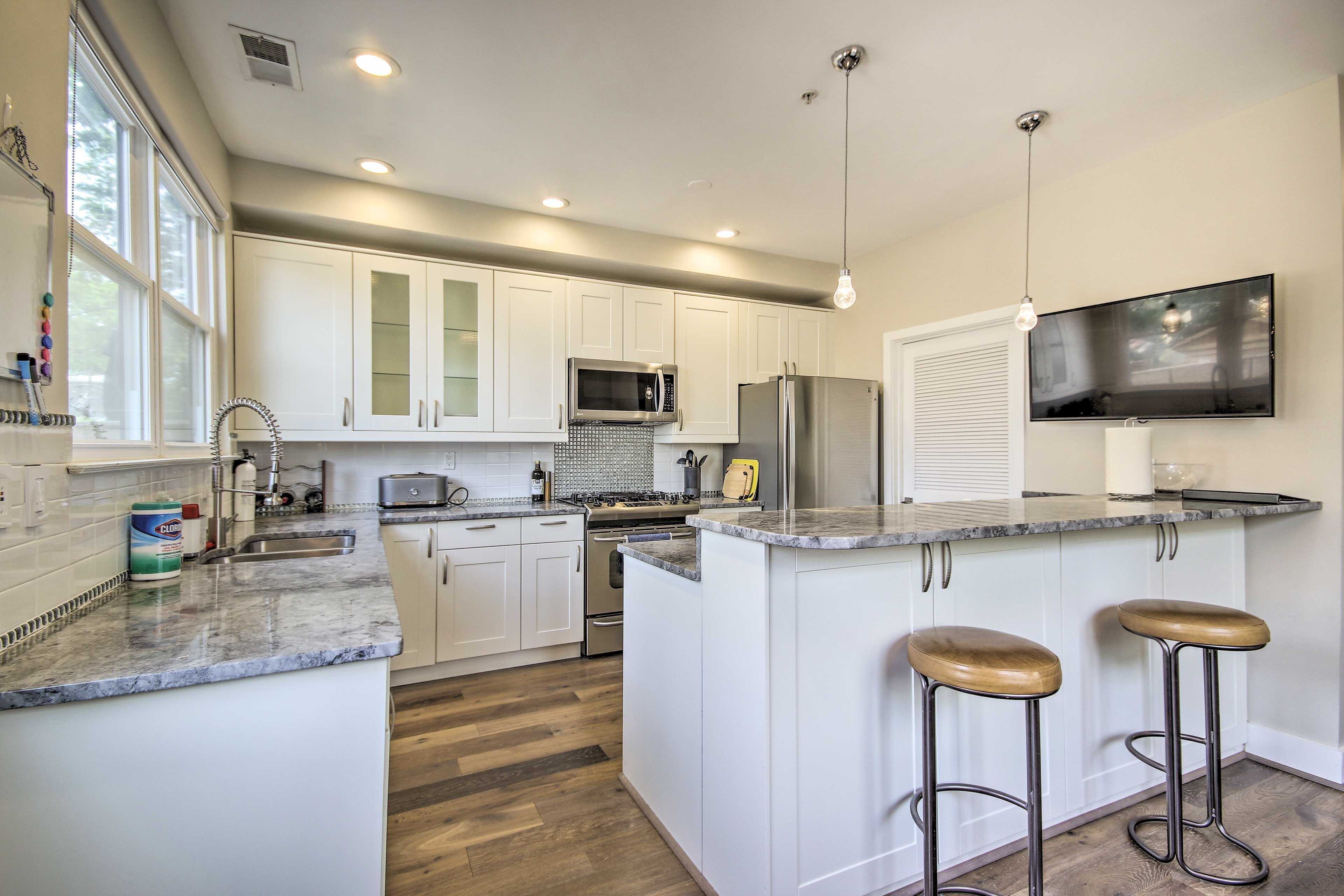 A modern kitchen with white cabinets, stainless steel appliances, a granite countertop, and two bar stools.
