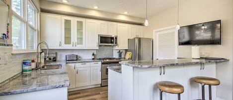 A modern kitchen with white cabinets, stainless steel appliances, a granite countertop, and two bar stools.