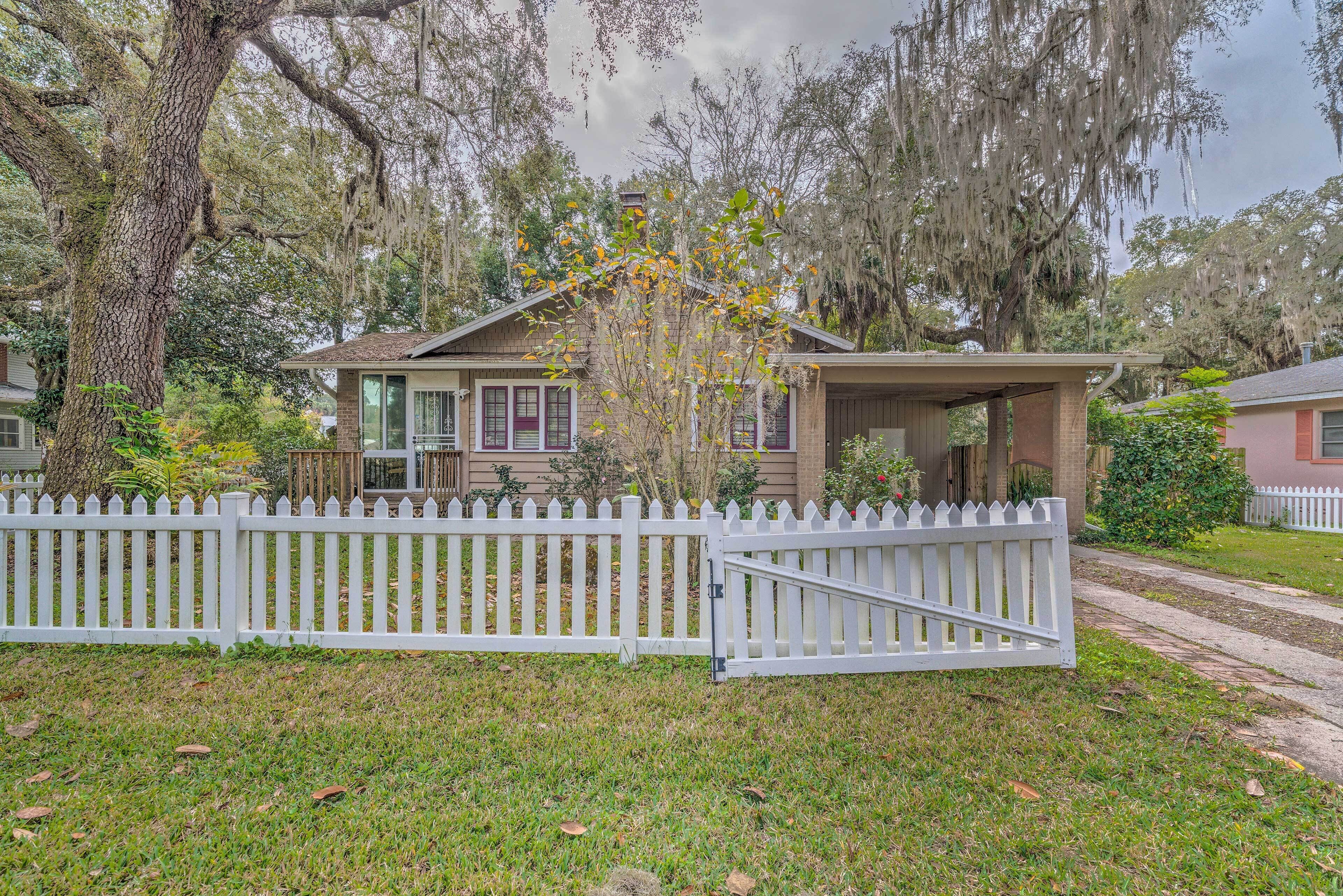 A house with a porch, a white picket fence, and a large tree with Spanish moss.