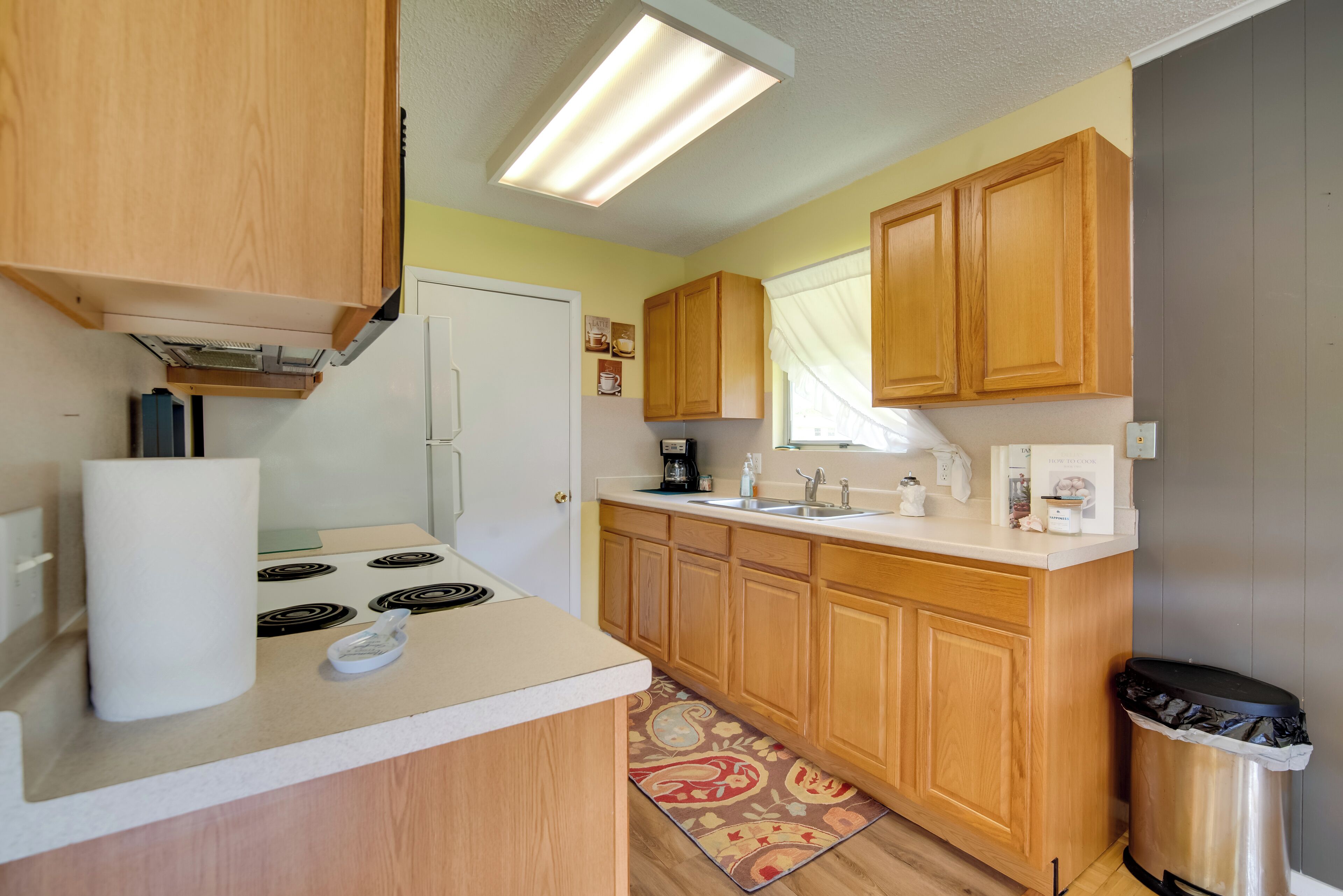 A compact kitchen with wooden cabinets, a white countertop, a built-in stove, a sink, and a trash can.