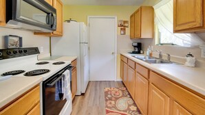 A compact kitchen with wooden cabinets, a white refrigerator, a microwave, a stove, and a sink. - Docks + Balcony: Peaceful River Abode in Dunnellon (Dunnellon)