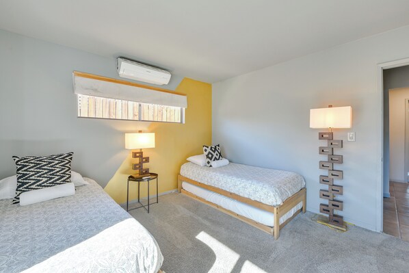 A bedroom with two beds, a bedside table with a lamp, an air conditioner, and a wall-mounted shelf. - Joshua Tree Vacation Home w/ Private Hot Tub! (Joshua Tree)
