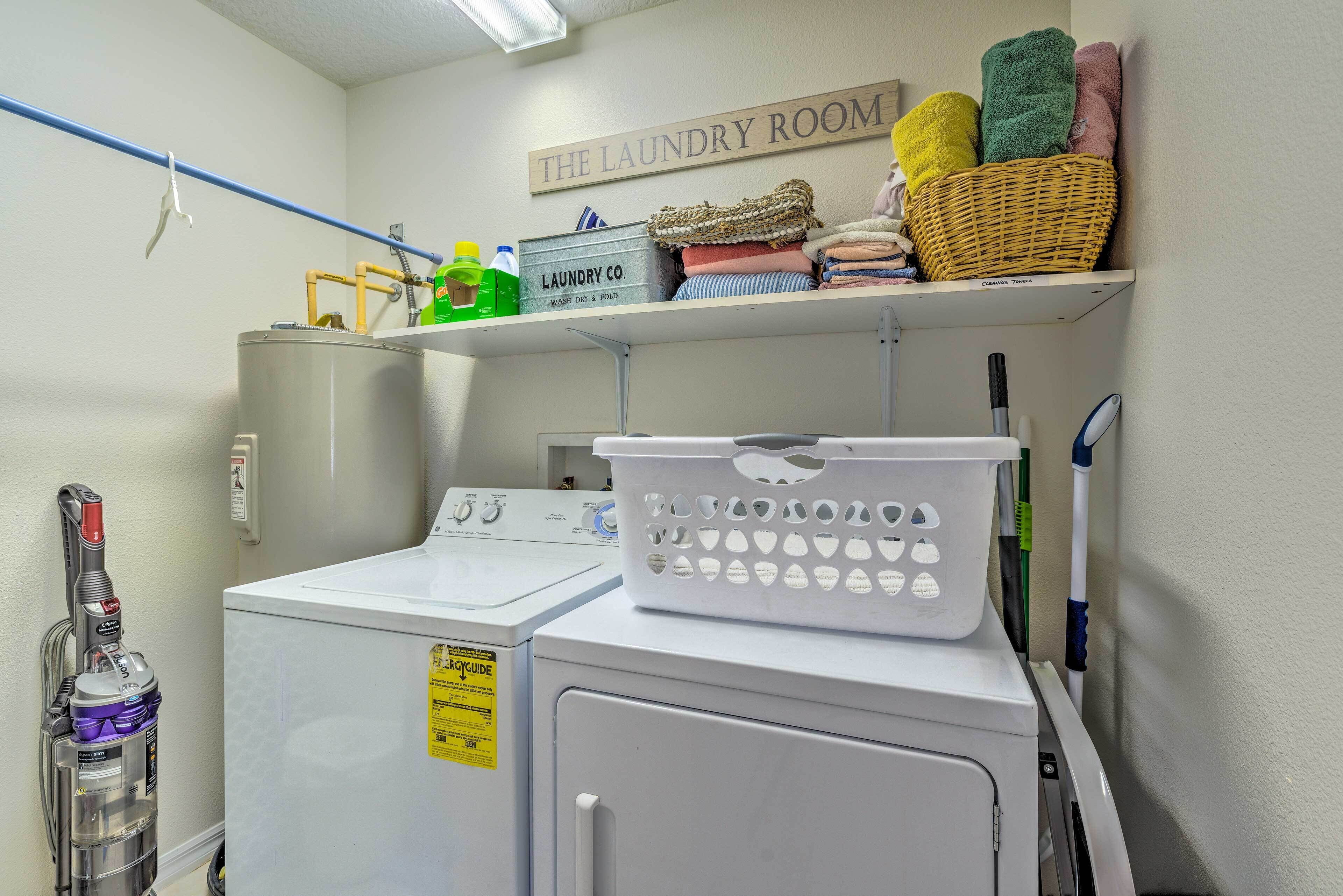 A laundry room with a washing machine, dryer, and a shelf with folded towels and laundry baskets.