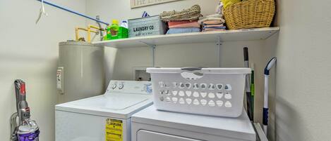 A laundry room with a washing machine, dryer, and a shelf with folded towels and laundry baskets.