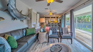 A spacious living room with a large fish mounted on the wall, a ceiling fan, and a view of the kitchen and outdoor deck. - Withlacoochee River House w/ Dock + Kayaks! (Inglis)