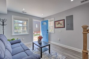 Un salon avec une porte bleue, un canapé gris et une petite table sur laquelle se trouve un vase.