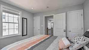 Une chambre avec un grand lit, une fenêtre avec des stores et une porte donnant sur une autre pièce.