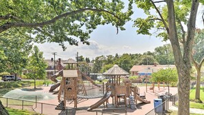 Ein Spielplatz mit verschiedenen Spielgeräten, umzäunt und von Bäumen gesäumt.