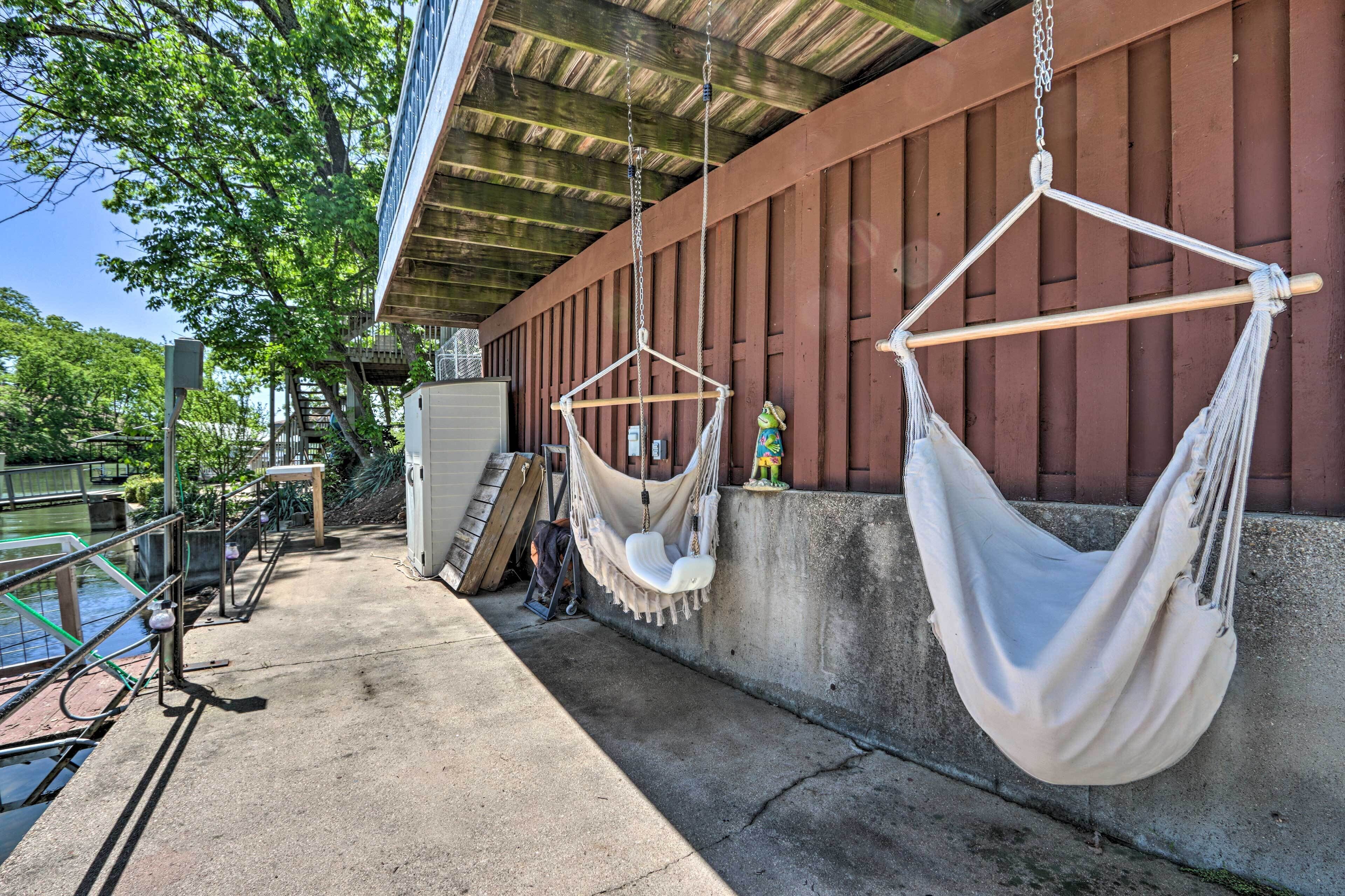 A concrete patio with two white hammocks hanging from a wooden beam, a metal railing, and a concrete wall with a window.