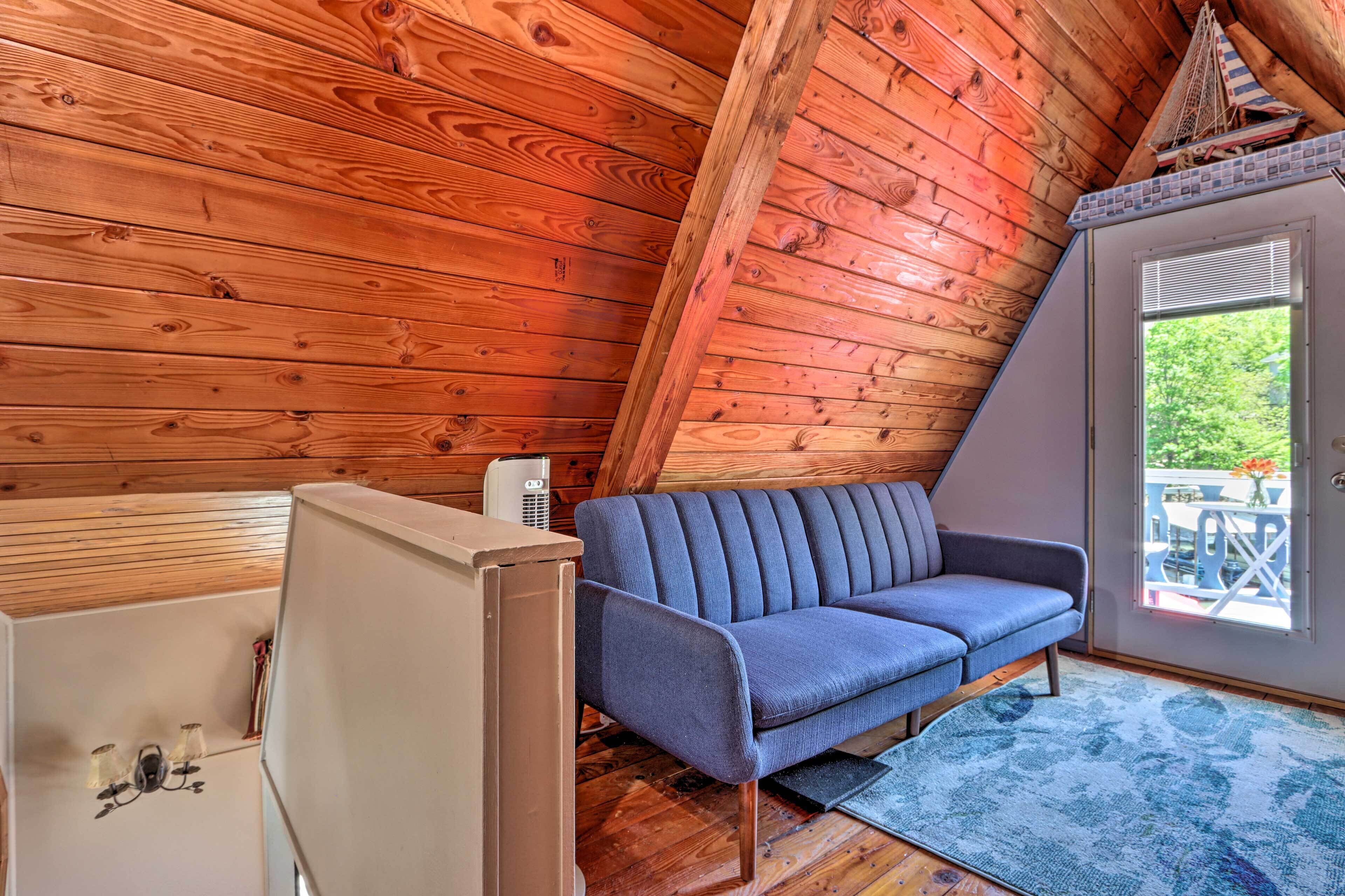A wooden cabin interior with a blue sofa, a white cabinet, and a window with a view of greenery outside.