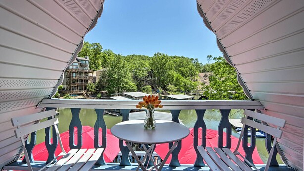 A balcony with a table and chairs, a vase with flowers, and a view of a river and buildings.