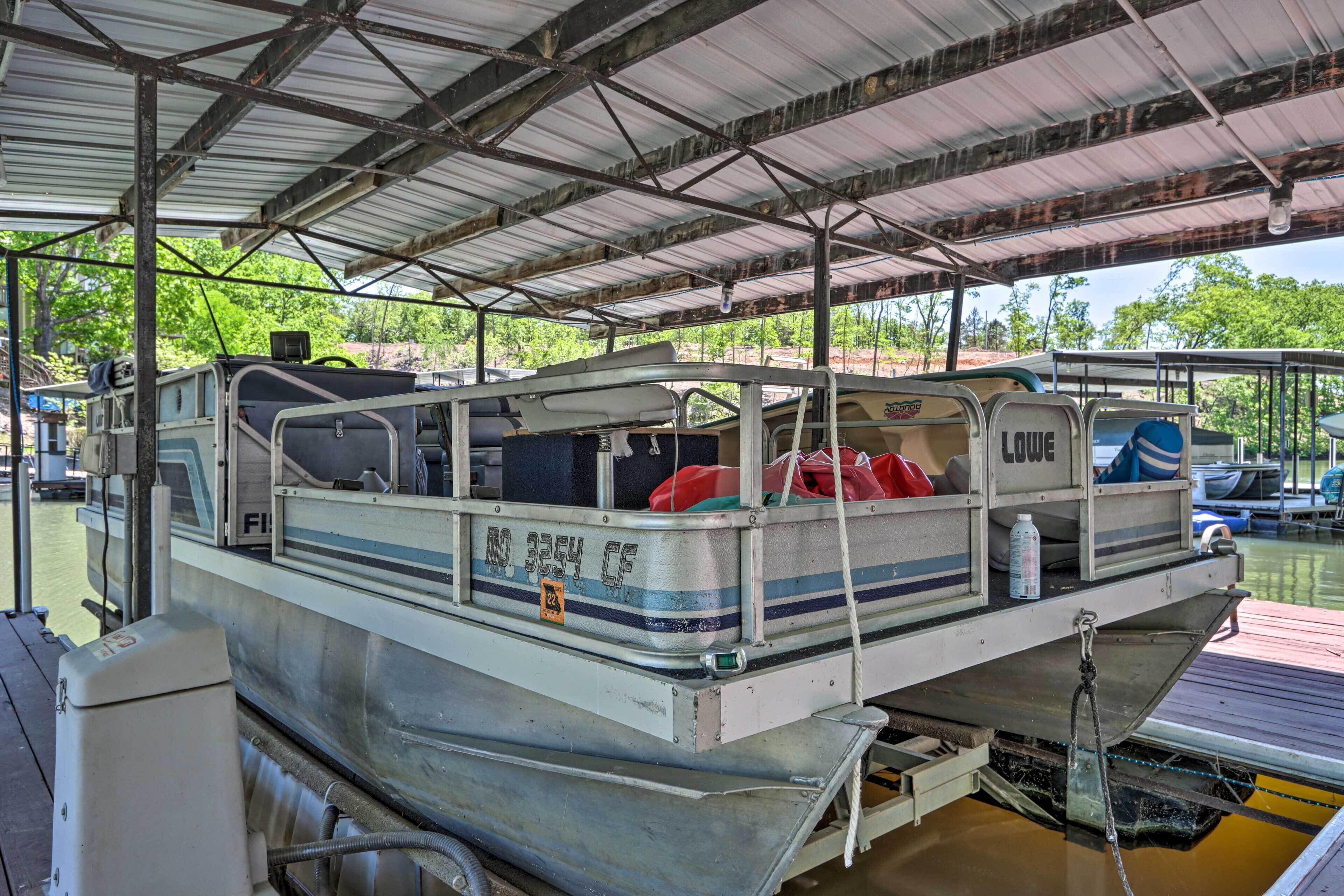 A stationary boat docked at a covered pier with a metal roof, equipped with a motor, seating, and storage compartments.