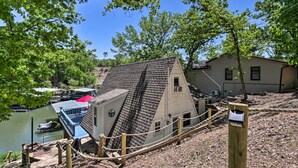 A house with a steep roof, a dock with a covered boat, and a small building with a sign.