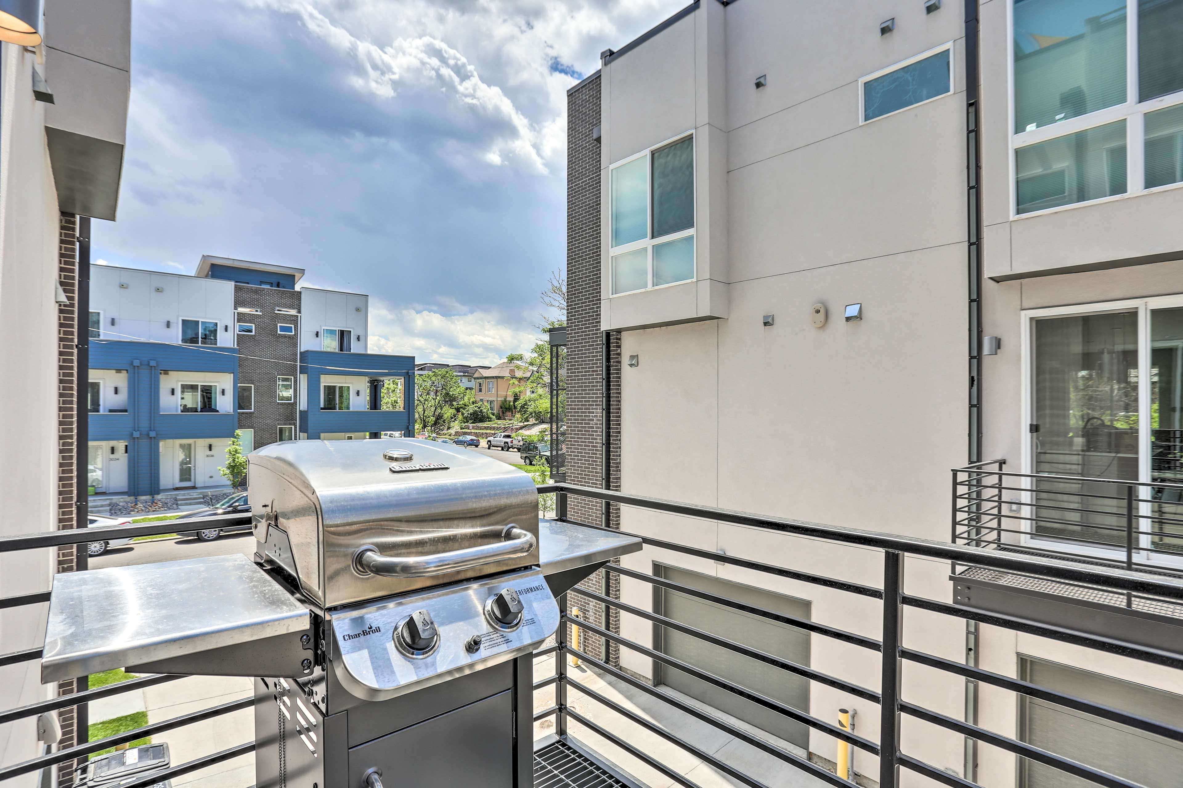 A balcony with a stainless steel grill, a metal railing, and a view of modern apartment buildings.