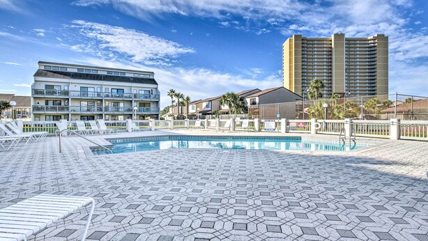 Un espace piscine d’hôtel avec un motif géométrique en mosaïque, des chaises longues et un grand bâtiment en arrière-plan.