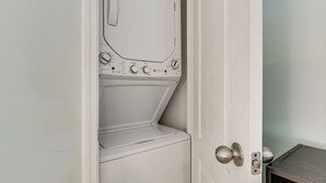 A white door with a built-in washer and dryer, a metal handle, and a small table beside it. - 1st-floor Resort Condo in PCB - Walk to Beach! (Panama City Beach)