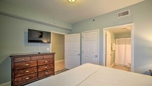 A bedroom with a bed, dresser, TV, and two doors leading to a bathroom. - 18th-floor PCB Resort Condo w/ Amazing Gulf View! (Panama City Beach)