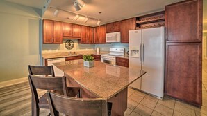 A kitchen with wooden cabinets, a granite countertop, a central island with chairs, a microwave, a stove, and a refrigerator. - 18th-floor PCB Resort Condo w/ Amazing Gulf View! (Panama City Beach)