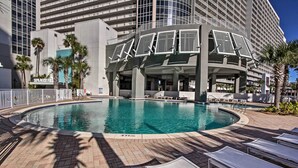 A hotel pool area with a circular pool, lounge chairs, and palm trees. - 18th-floor PCB Resort Condo w/ Amazing Gulf View! (Panama City Beach)