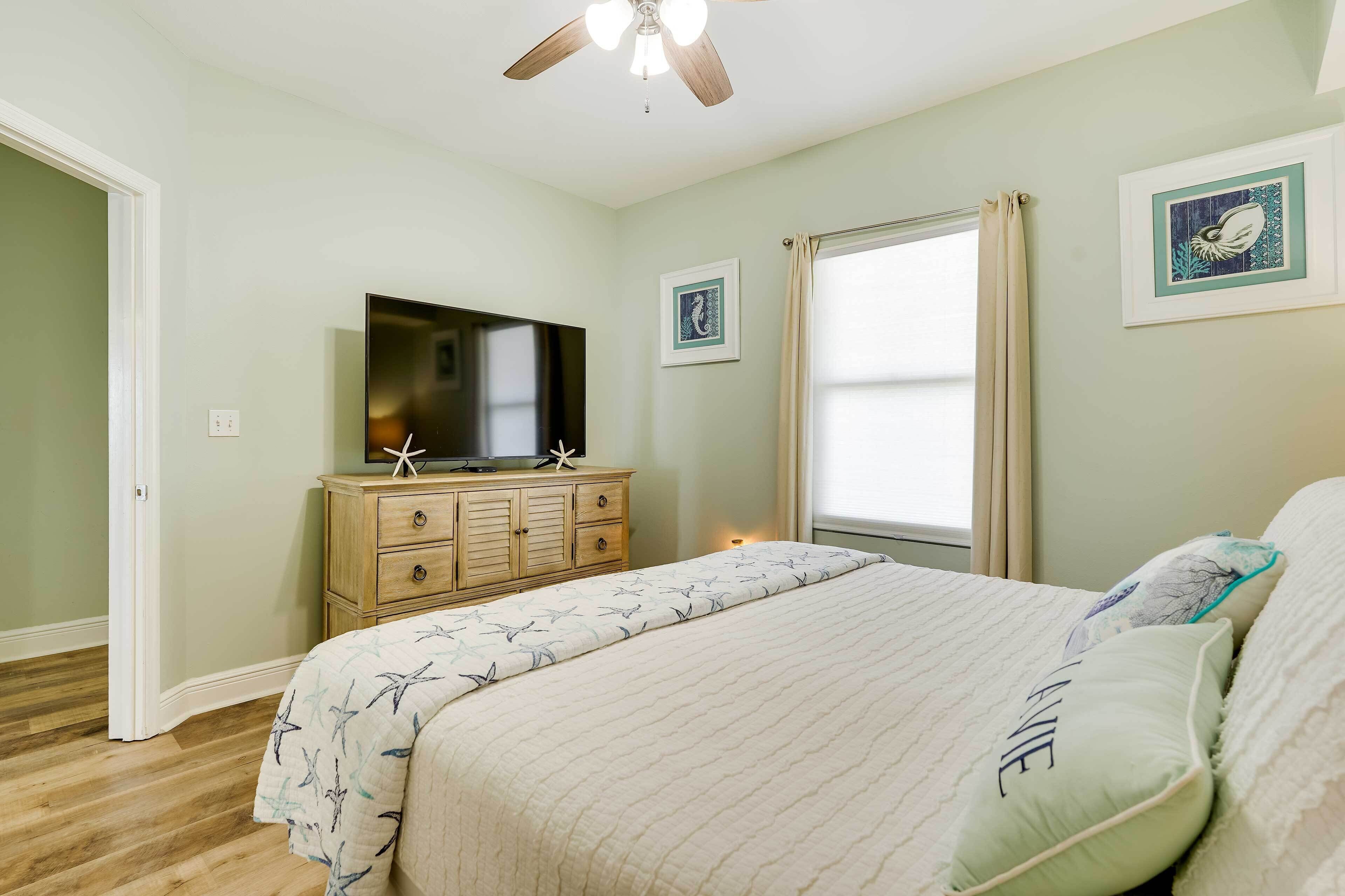 A bedroom with a bed, a dresser, a television, and a window with curtains.