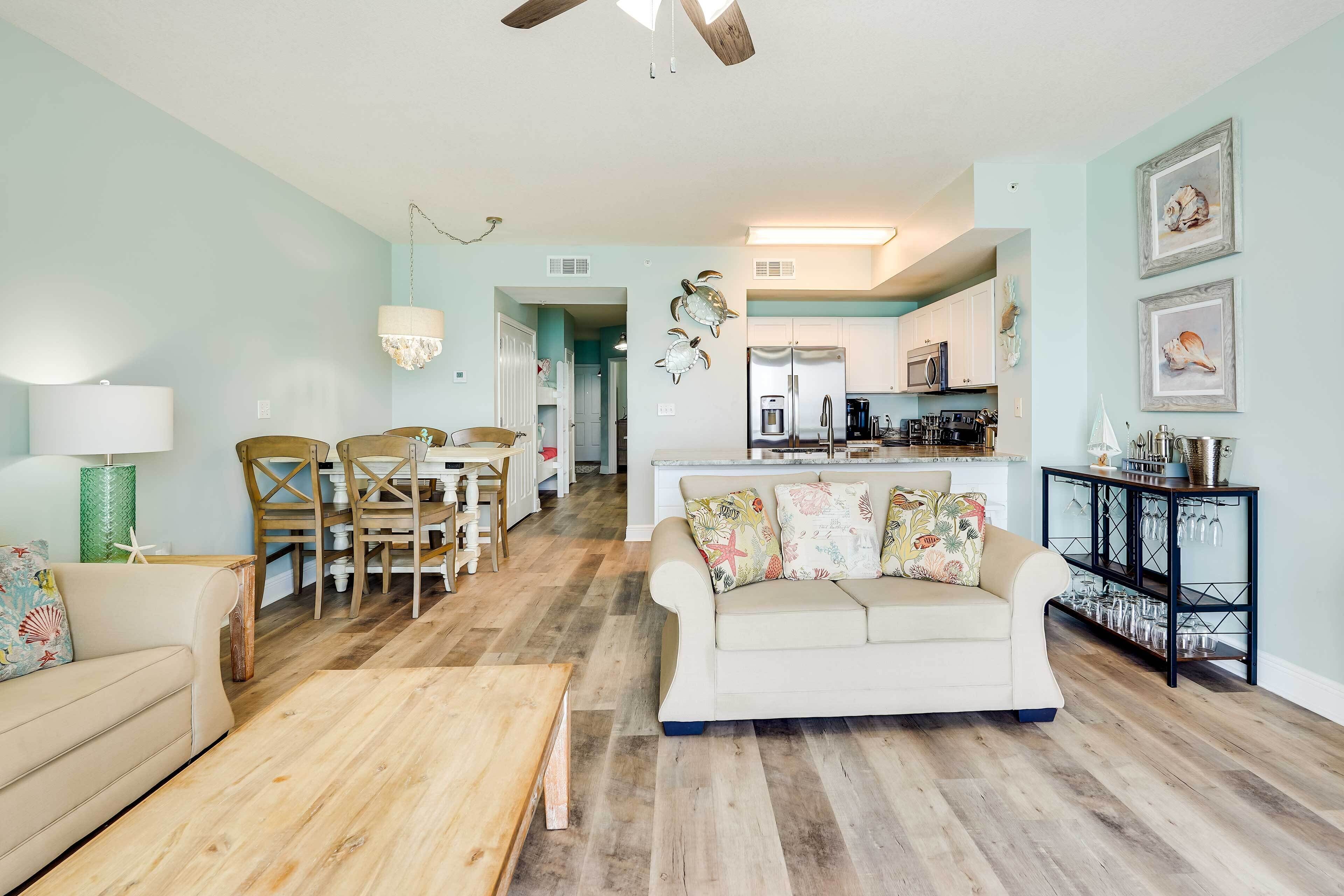 A spacious living room with a wooden floor, a beige sofa, a wooden coffee table, and a dining area with chairs and a table.