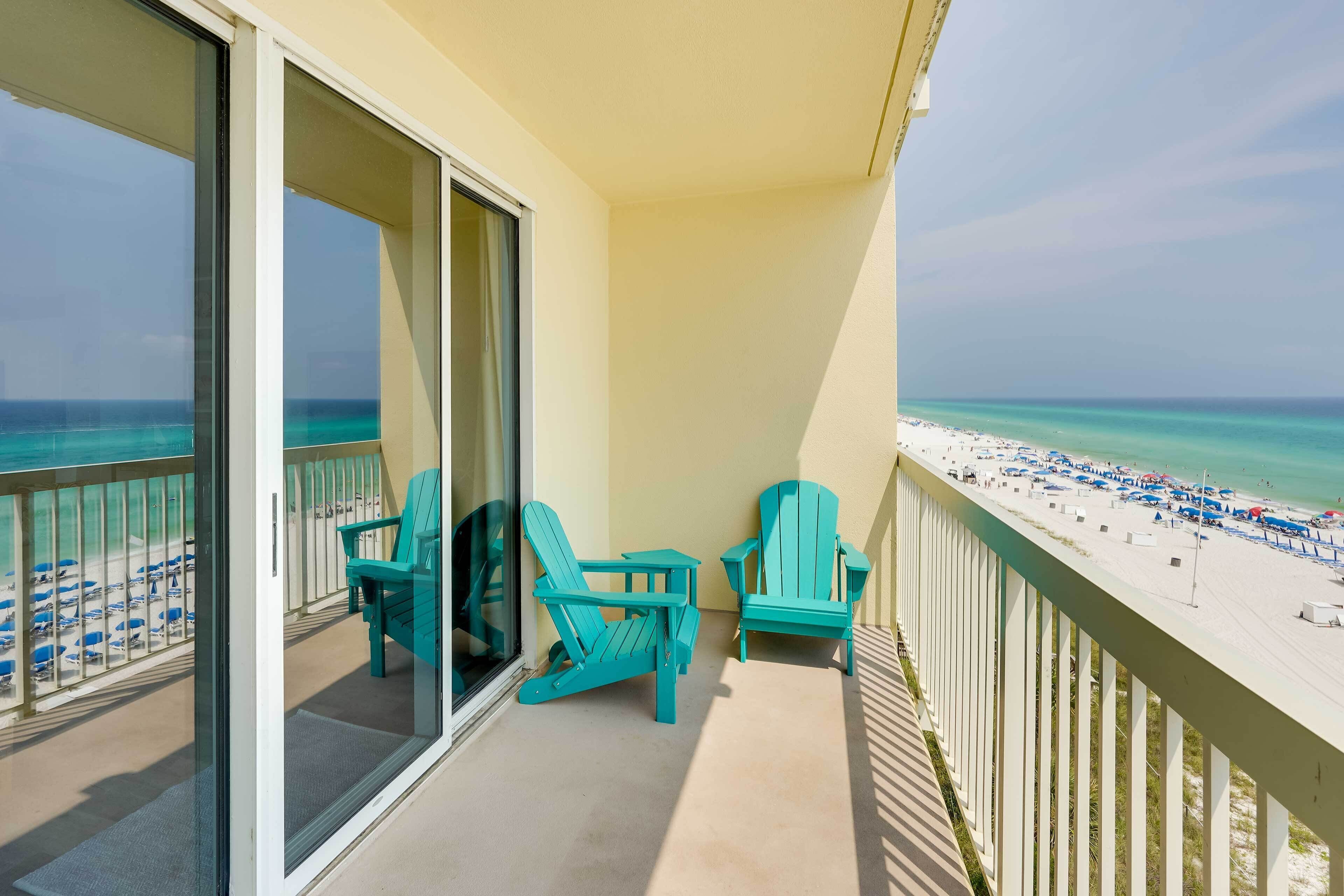 A balcony with two turquoise Adirondack chairs and a glass door leading to a beach view.