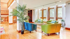 Un salon spacieux doté d’un parquet en bois, d’une grande plante en pot et de deux fauteuils verts.