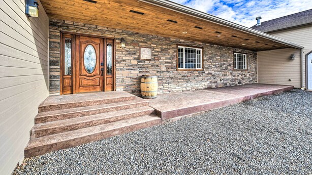A stone house with a wooden front door, steps leading to a covered porch, and a barrel on the porch. - The Vineyard Country Farm Home at Grand Valley (Grand Junction)