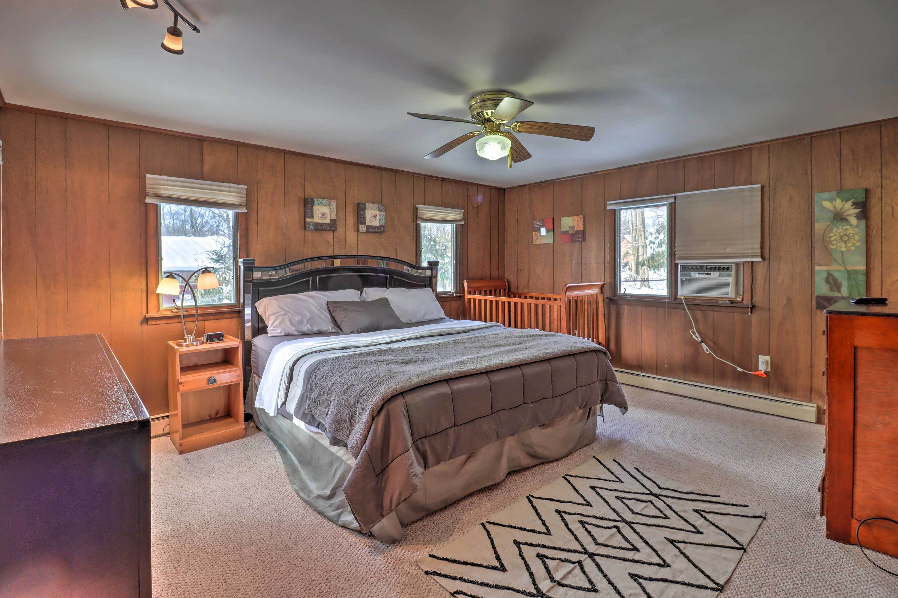 A bedroom with a bed, a ceiling fan, a window with blinds, and a wooden wall panel.