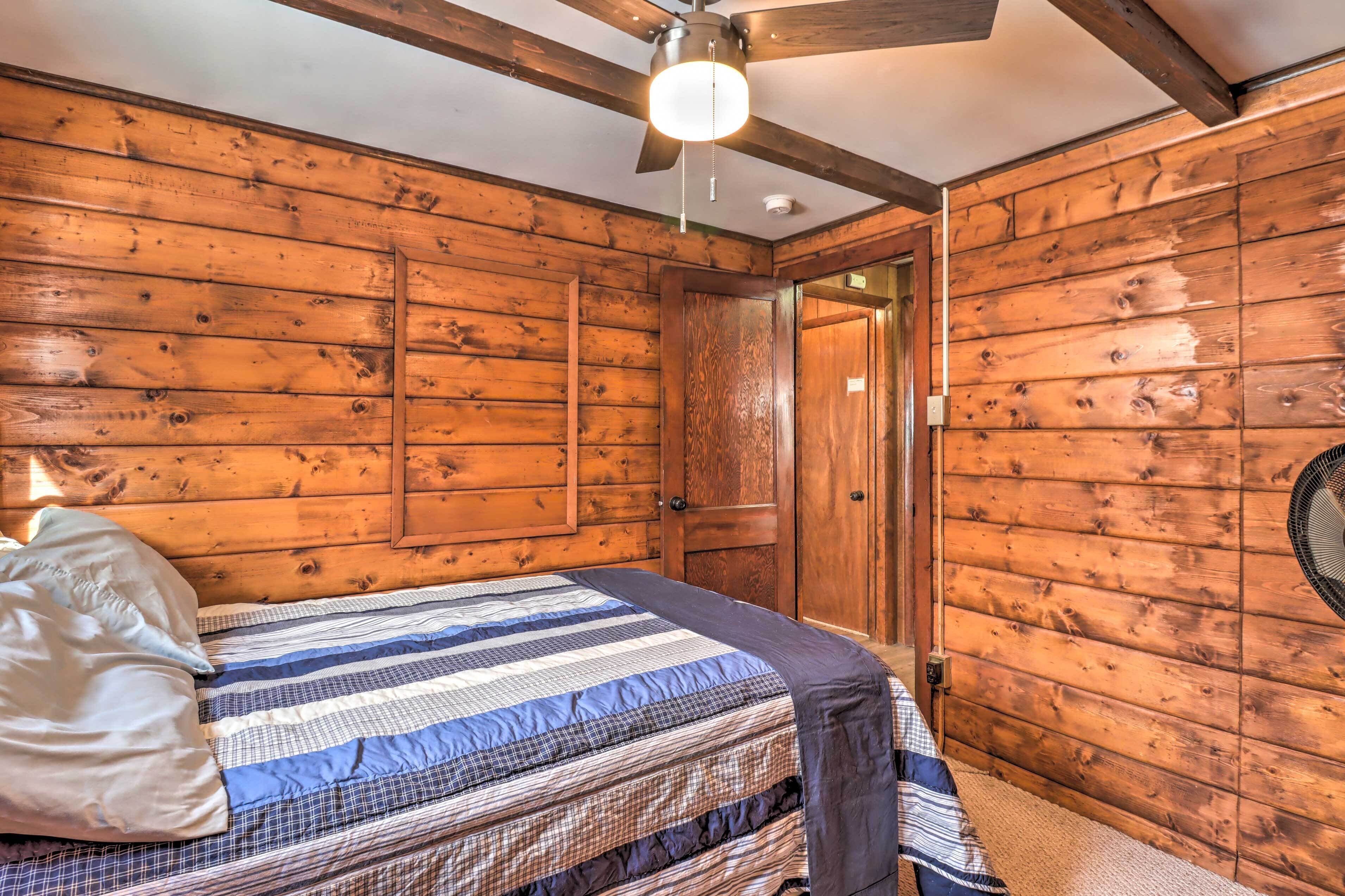 A wooden-paneled room with a bed, a ceiling fan, and a door.