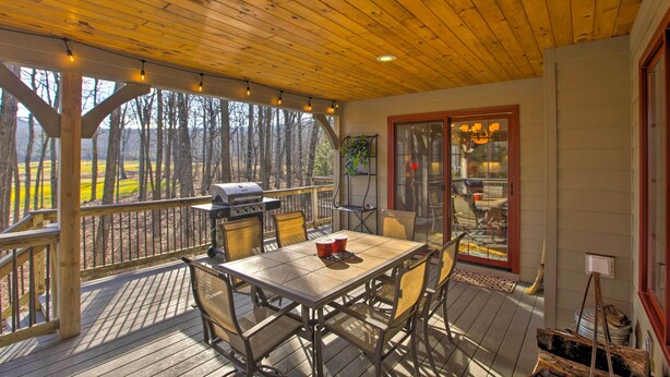 A covered deck with a wooden table and chairs, a grill, and a view of trees. - Spacious Wintergreen Resort Home w/ Hot Tub! (Nellysford)