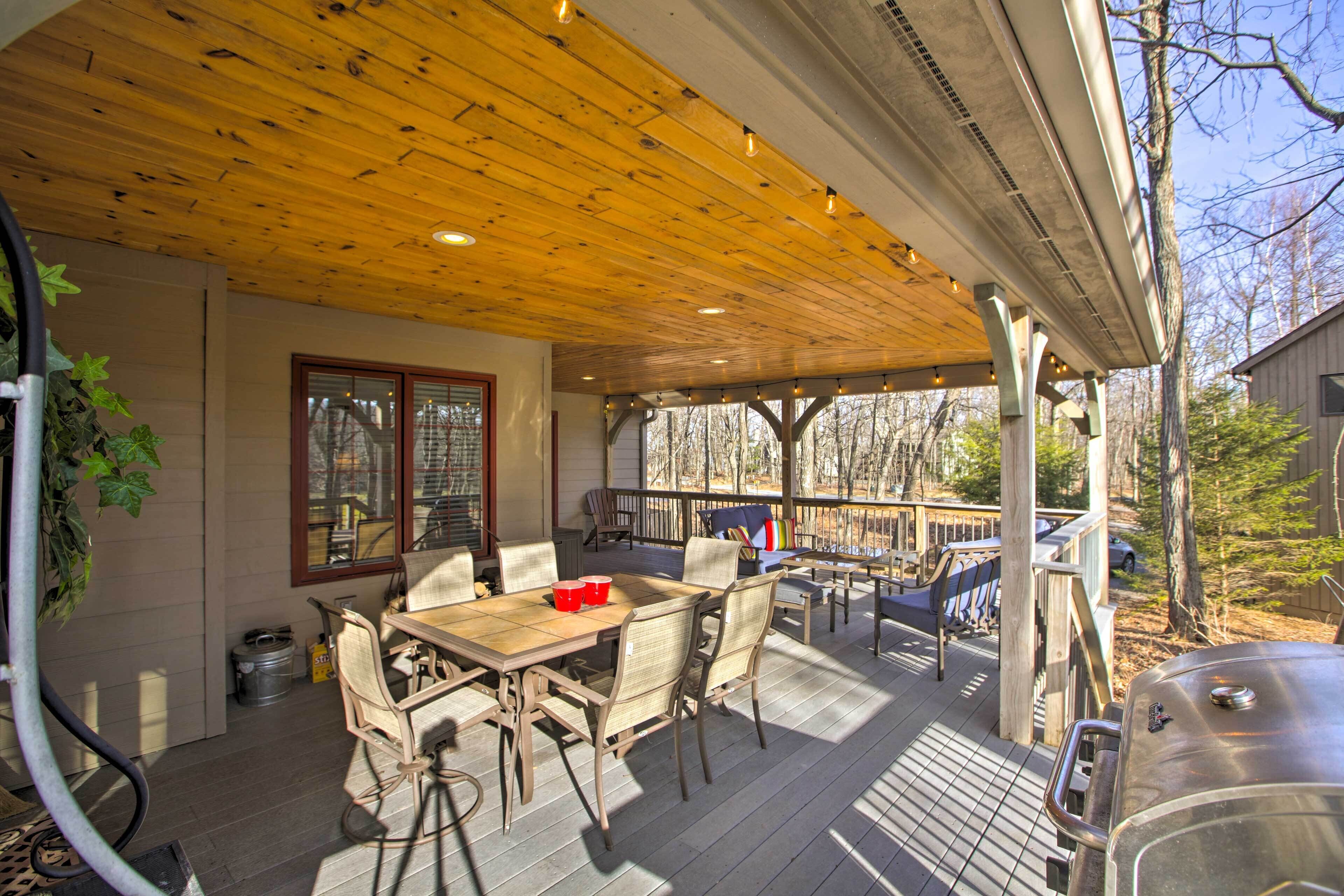 A covered outdoor patio with a wooden deck, a dining table with chairs, and a barbecue grill.