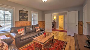 A cozy living room with a leather sofa, a wooden coffee table, and a red patterned rug. A sign on the wall reads "Moose Creek Lodge." - Spacious Wintergreen Resort Home w/ Hot Tub! (Nellysford)