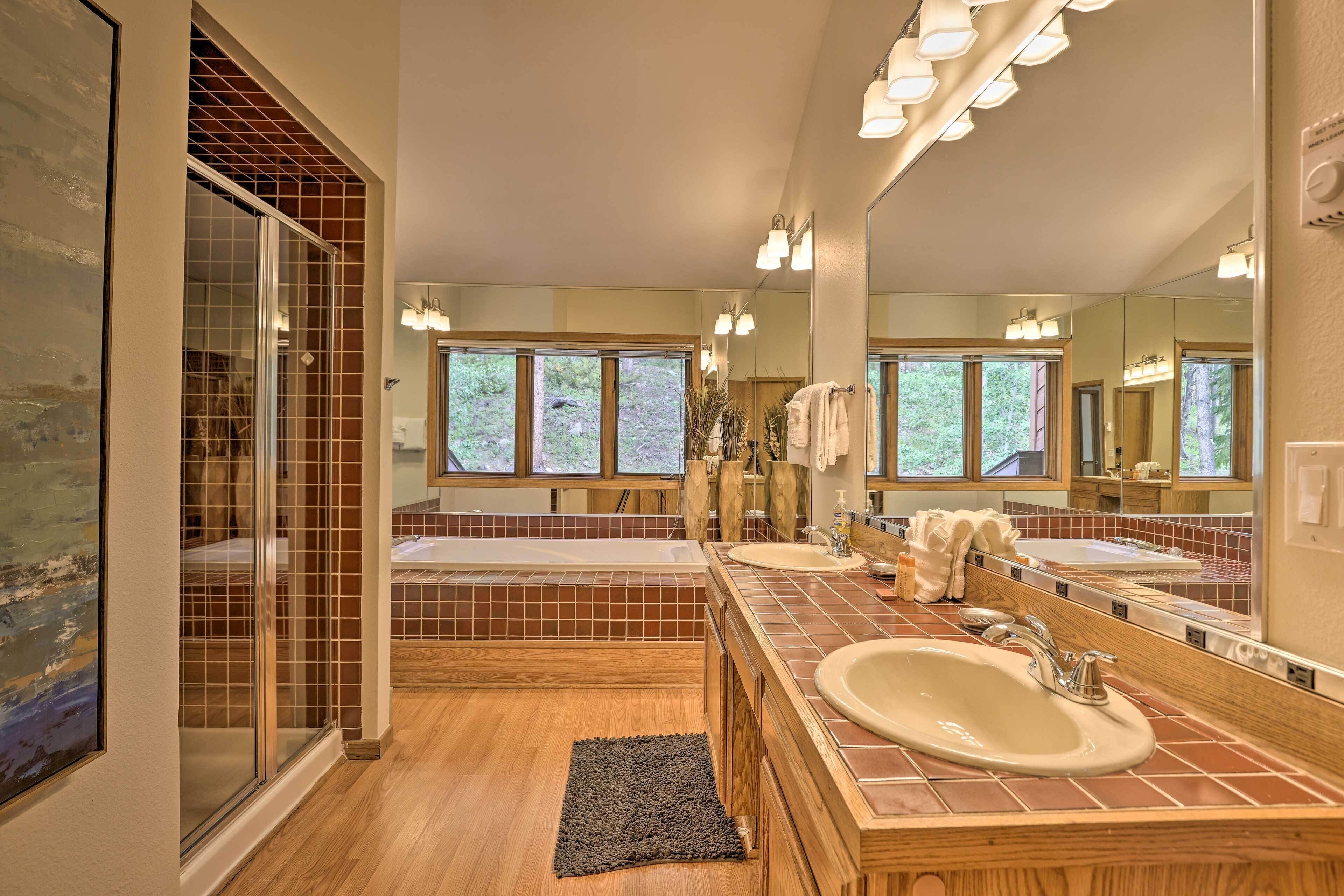 A modern bathroom with a large mirror, two sinks, a bathtub, and a glass shower enclosure.