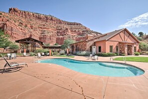 Un área de piscina con sillones de descanso, una zona de estar cubierta y un edificio con fachada de piedra.
