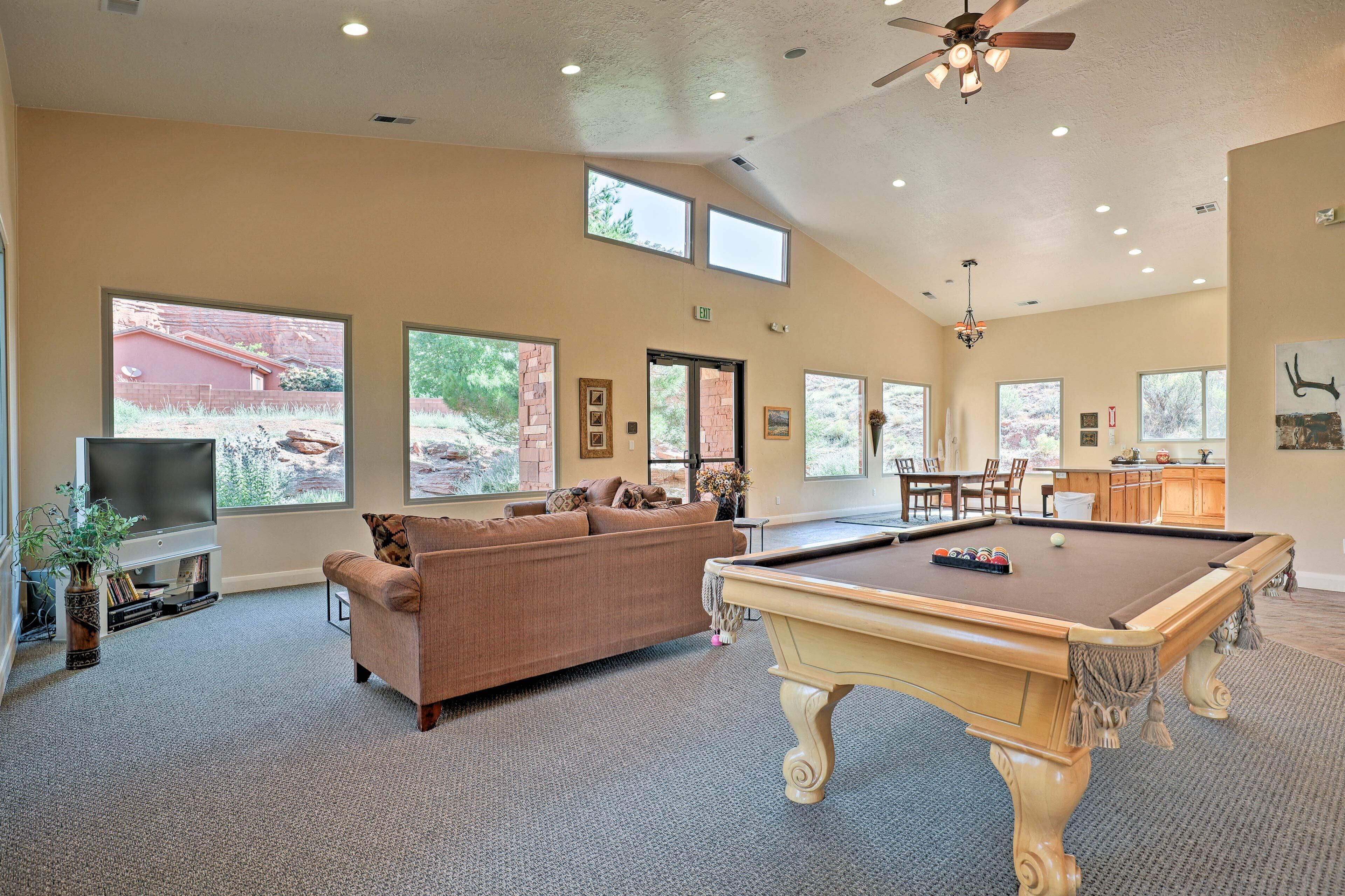 A spacious living area with a pool table, comfortable seating, and large windows offering views of the outdoors.