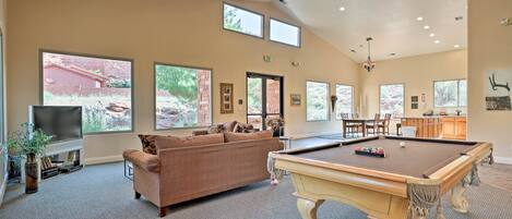 A spacious living area with a pool table, comfortable seating, and large windows offering views of the outdoors.