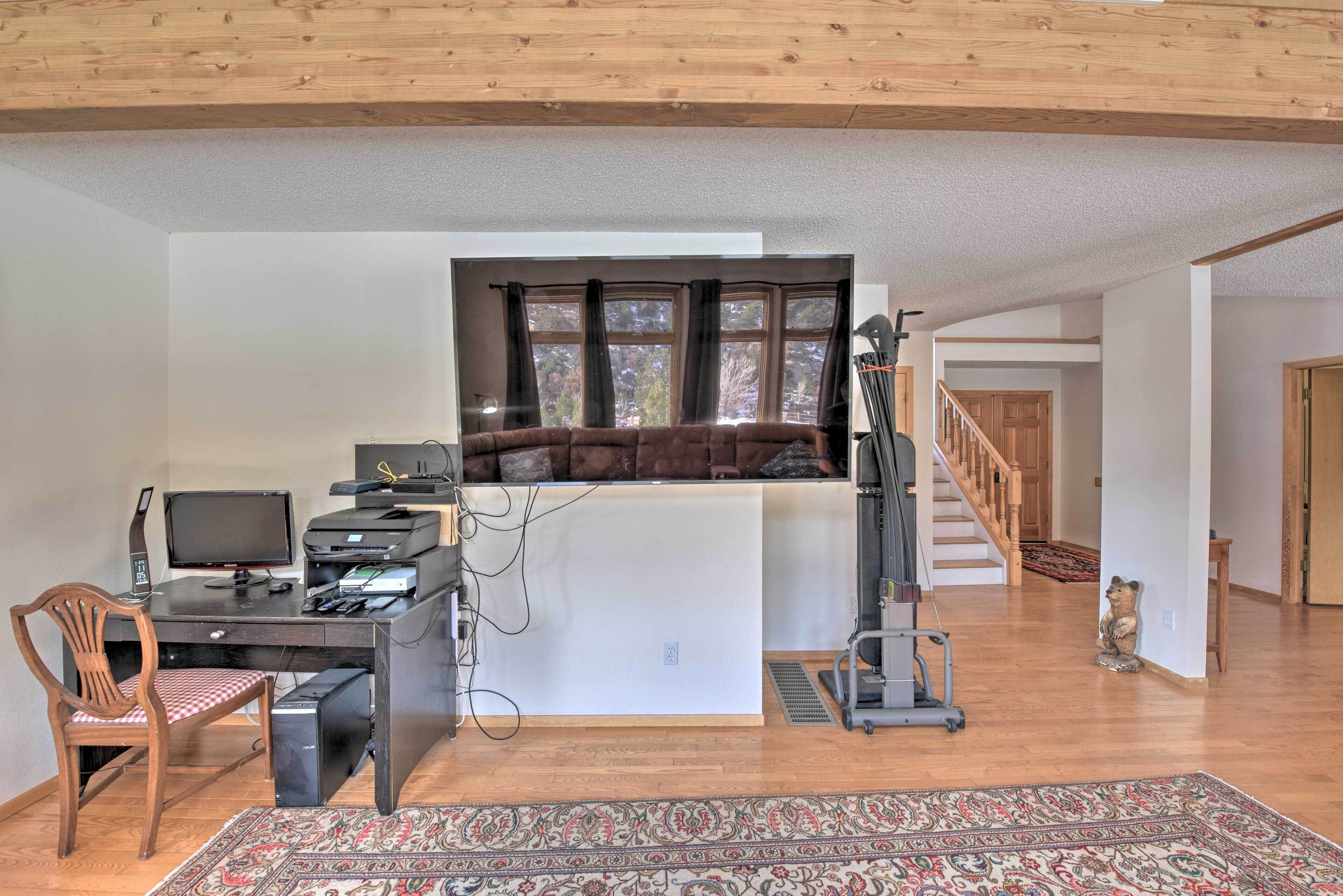 Et kontor med skrivebord, computer og stol, en sofa og et vindue med gardiner.