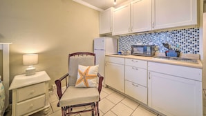 A compact kitchen with white cabinets, a microwave, and a small dining area with a chair and table. - Beachfront PCB Studio: Pool, Patio & Deck Access! (Panama City Beach)