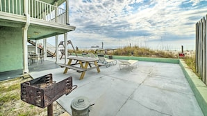 A covered patio with outdoor seating, a staircase leading to an upper deck, and a view of the beach and dunes. - Beachfront PCB Studio: Pool, Patio & Deck Access! (Panama City Beach)