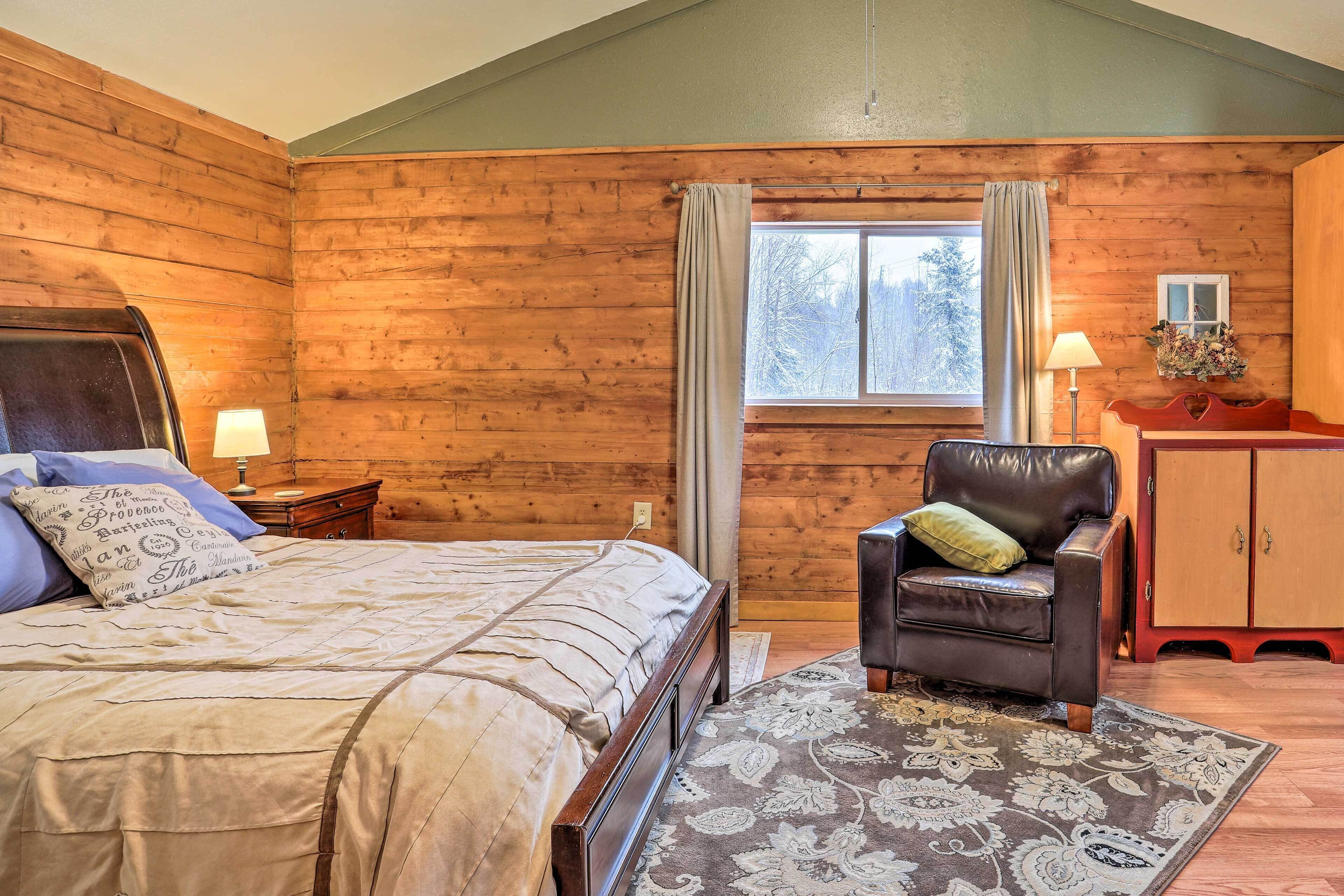 Una habitación de madera con cama, un sillón de cuero, un mueble pequeño y una ventana con cortinas.